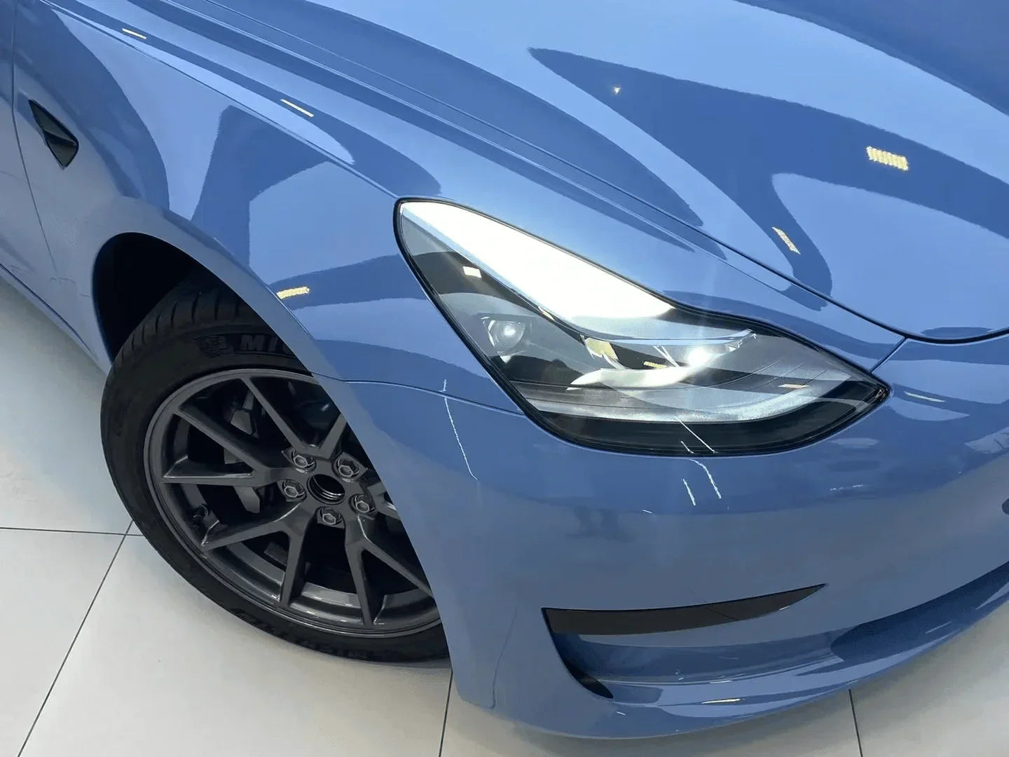 Close-up of a blue car's headlight and front wheel on a white background