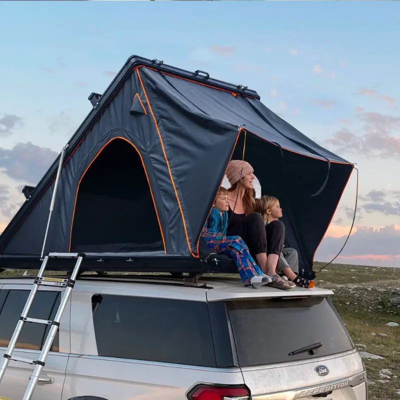 Two people sitting on a rooftop tent with a scenic background